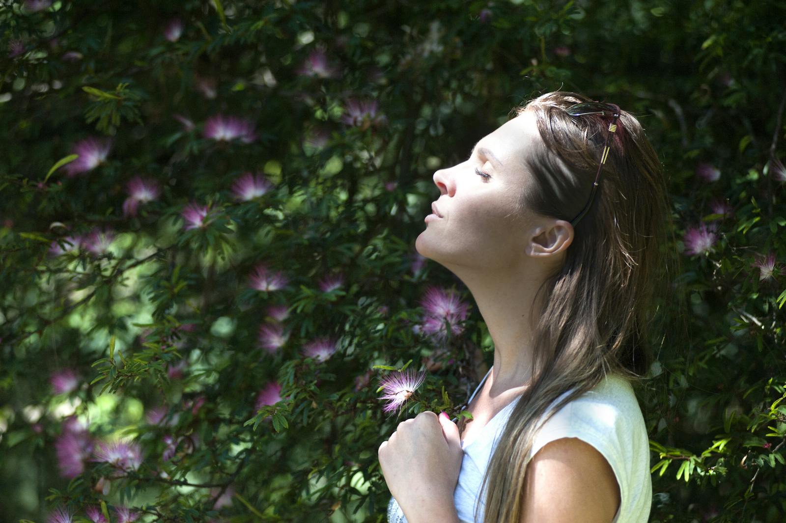 Mujer cerrando los ojos contra la luz del sol de pie cerca de una planta de flores de pétalos morados